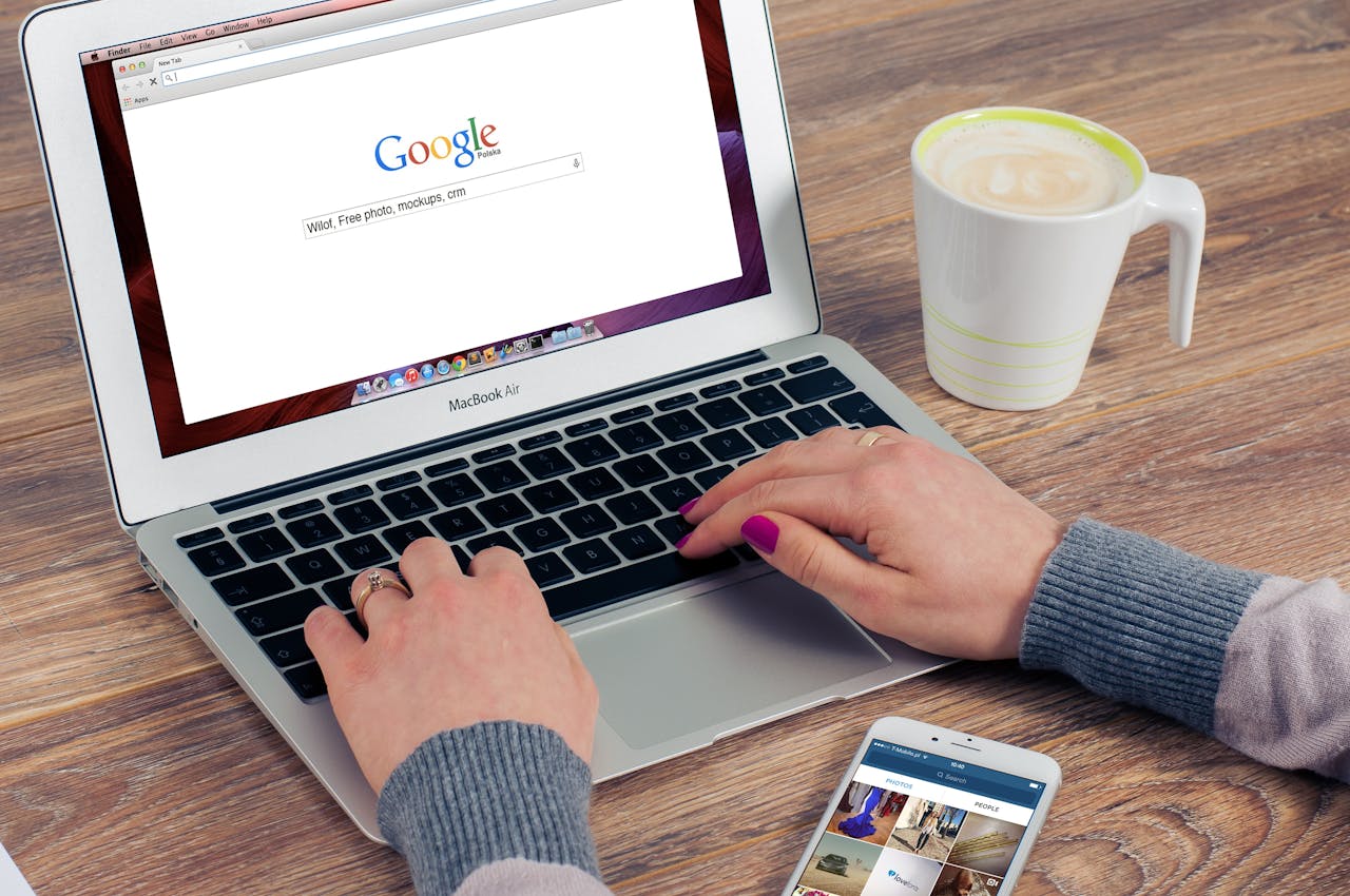home-img Hands typing on MacBook Air with Google search open, coffee nearby.